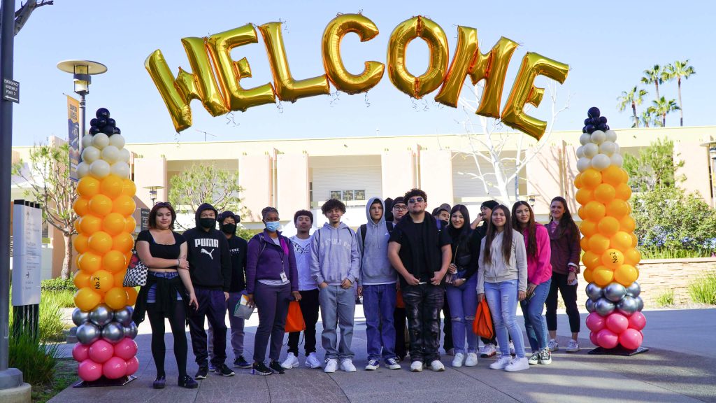 Group of students pose in front of a Welcome sign