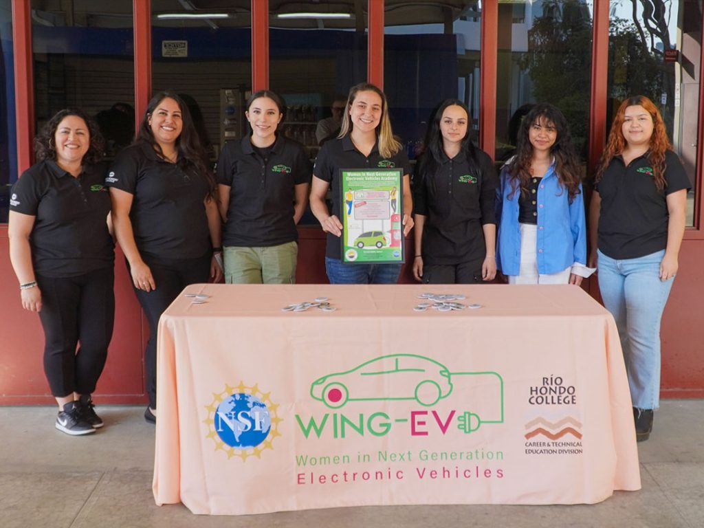 A group of women standing in front of a table with a Wing-EV logo