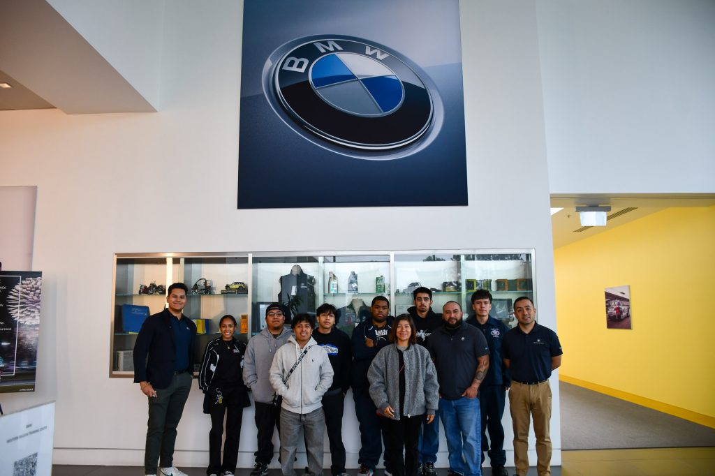 A group of people posing for a photo in a lobby under a large bmw logo, with branded merchandise displayed behind them.