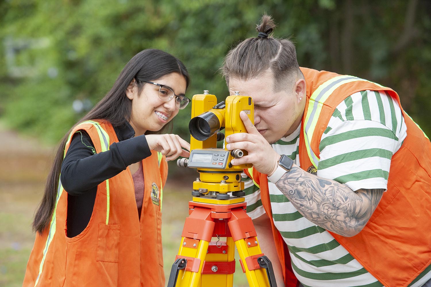 Two students wearing orange vests use a piece of architecture equipment