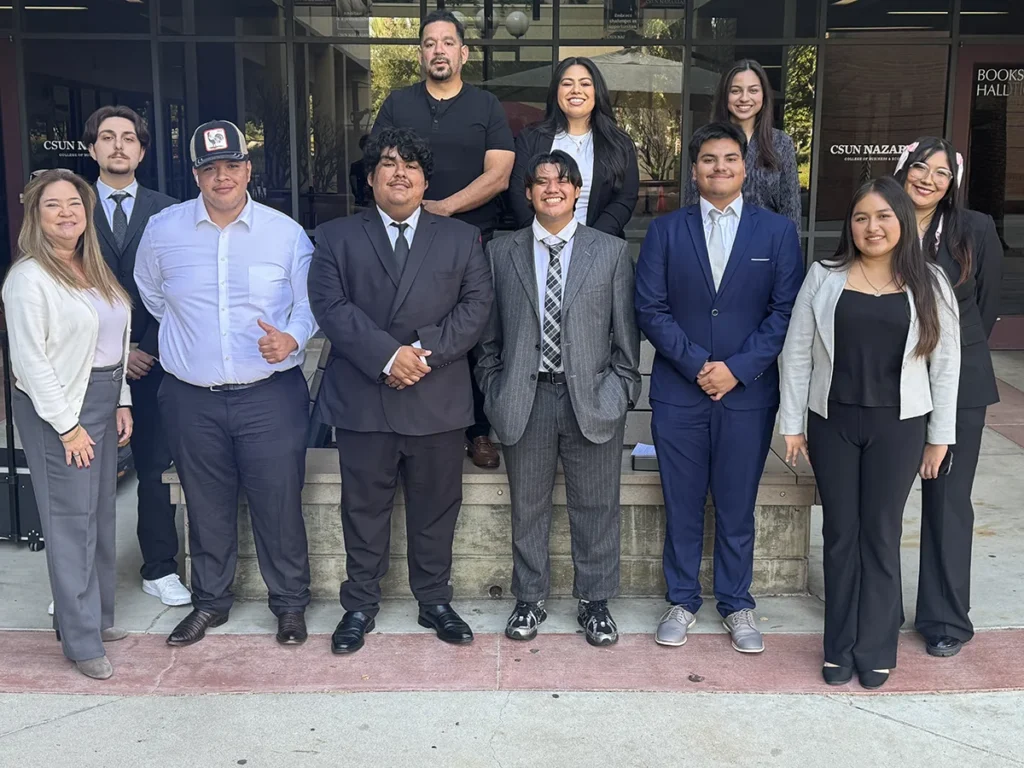 A group of eleven people, mostly dressed in business attire, stand and smile on steps outside a building with large glass doors.