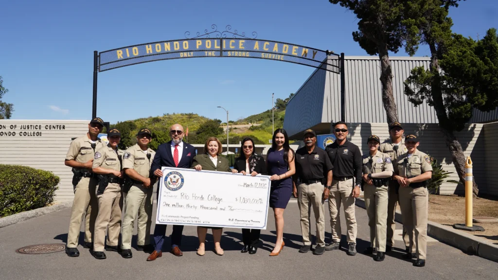 A group of people, including police officers and officials, stand in front of Rio Hondo Police Academy holding a large check for $1,000,000.
