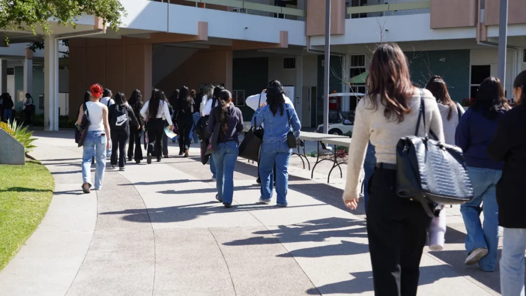 A group of people walk along a curved outdoor pathway beside a building on a sunny day.