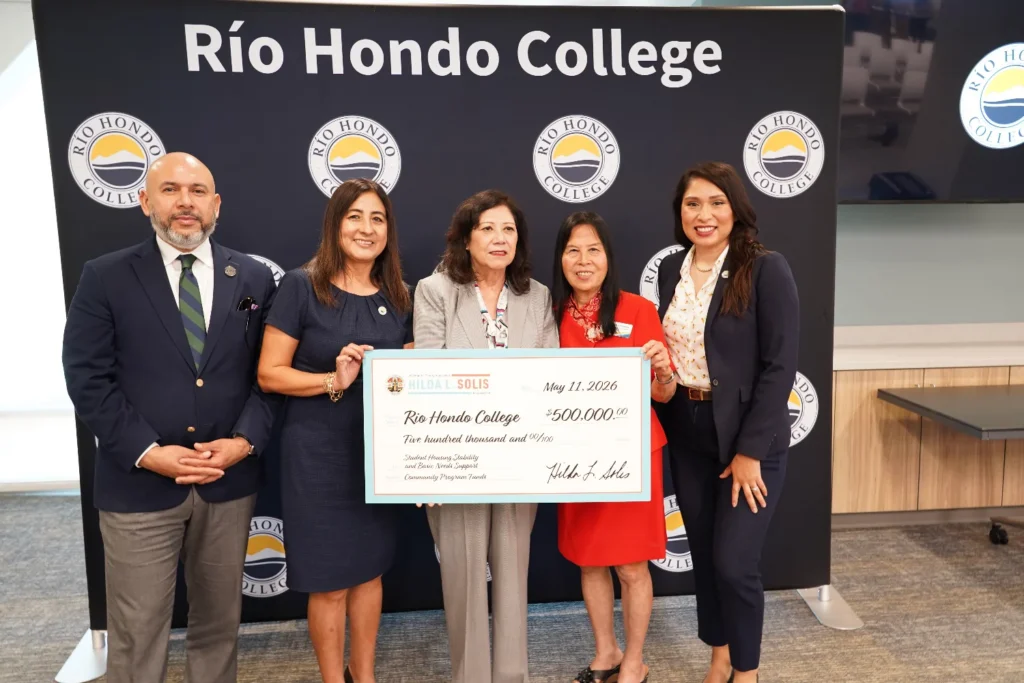 Five people stand indoors holding a large ceremonial check for $500,000 made out to Río Hondo College, with a Río Hondo College branded backdrop behind them.