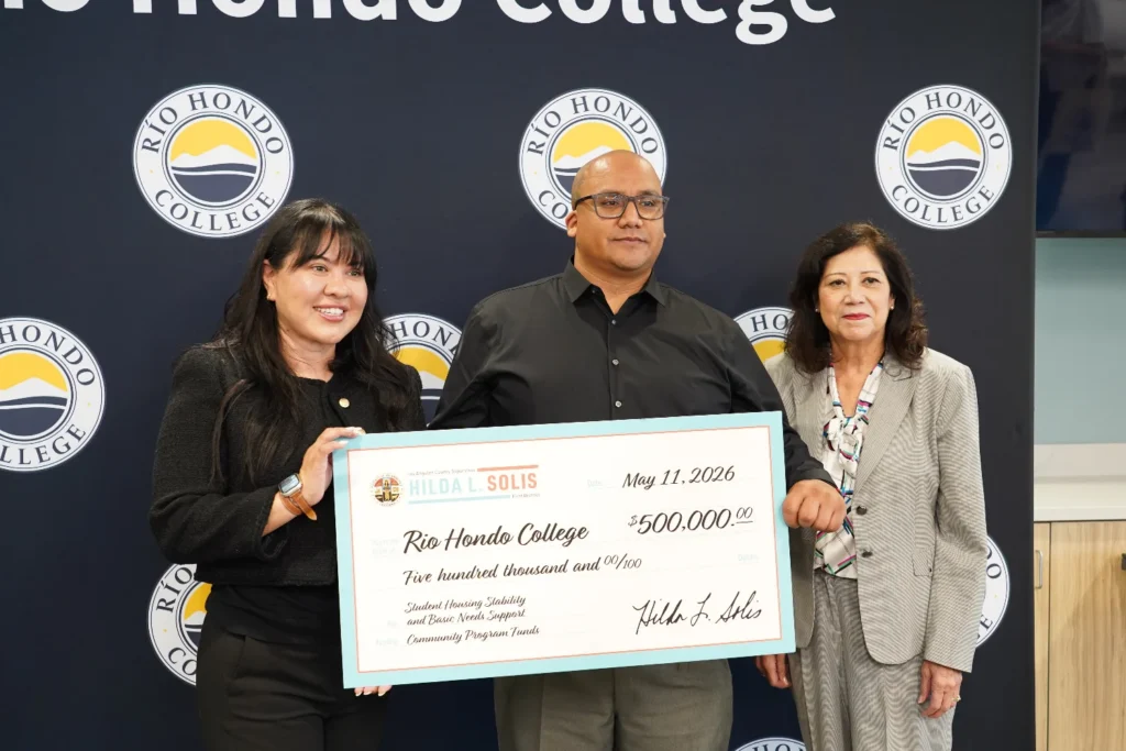 Three people pose in front of a Rio Hondo College backdrop, holding a large check for $500,000 made out to the college, dated May 11, 2026.