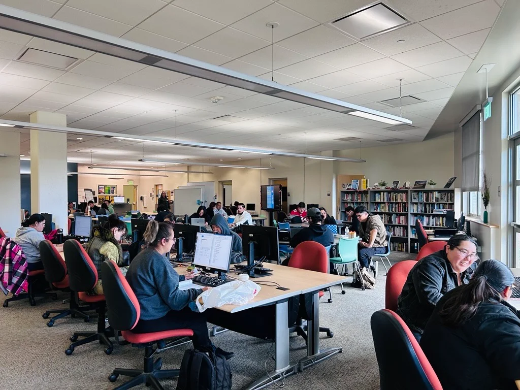 Students working at computers in a university library or computer lab.